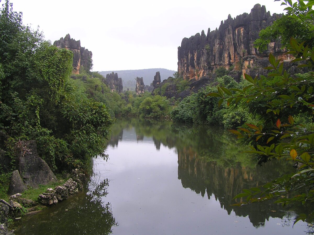 A still pond at Naigu Stone Forest with limestone cliffs and green hills reflected in it