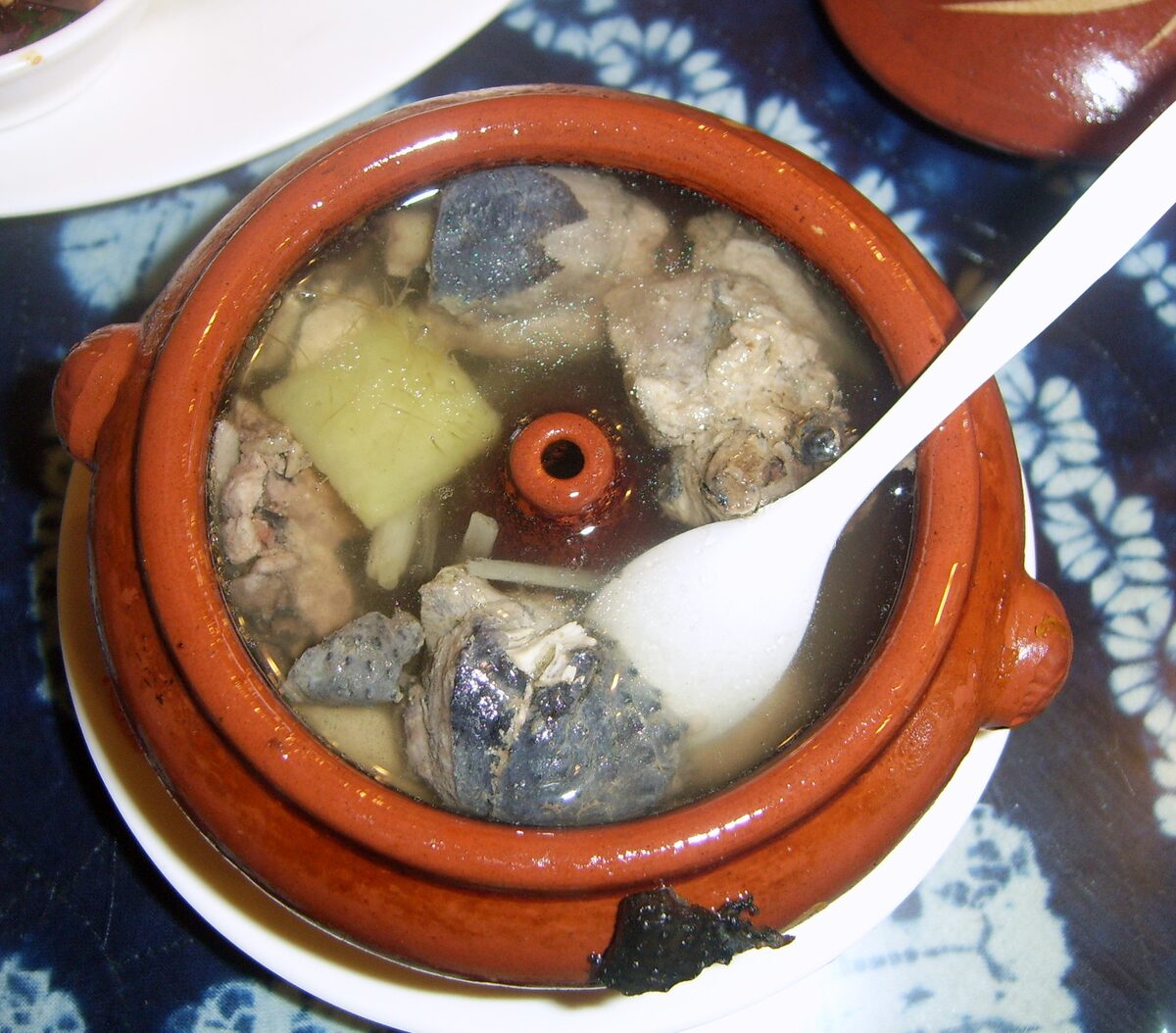 Steam pot chicken in a clay pot, with chicken pieces in broth and a white spoon