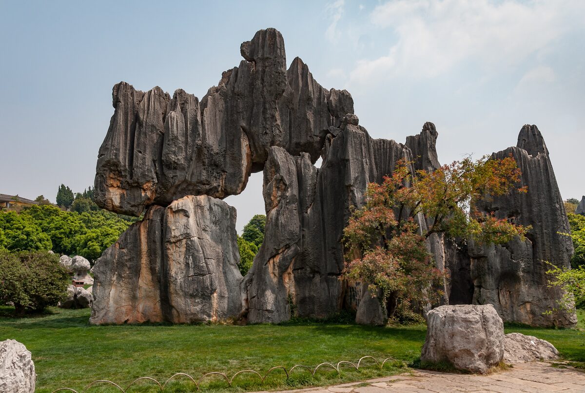 Gray limestone pillars forming a natural arch in the Stone Forest, with trees and a lawn