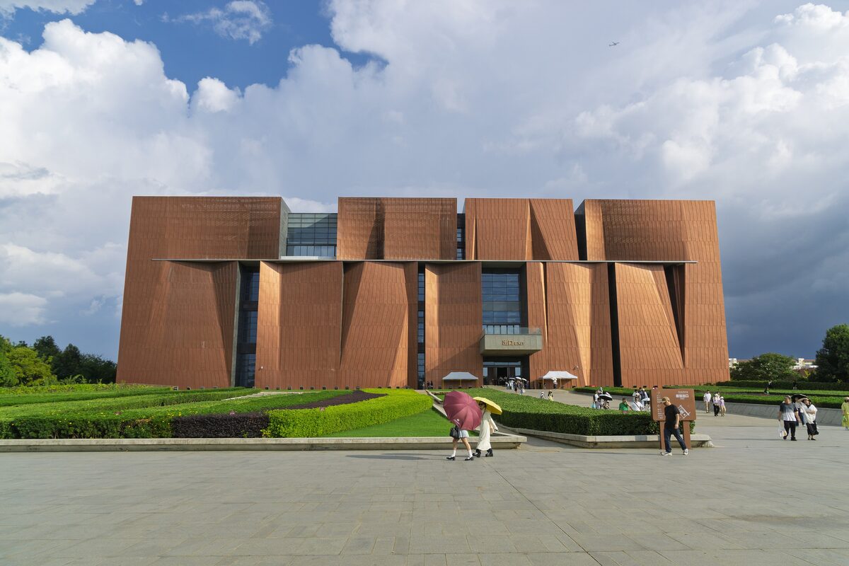 The terracotta-colored blocks of the Yunnan Provincial Museum under a blue sky, with visitors on the forecourt