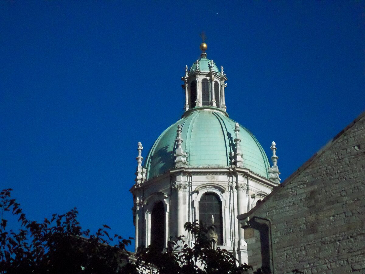 The green copper dome of Como Cathedral against a deep blue sky