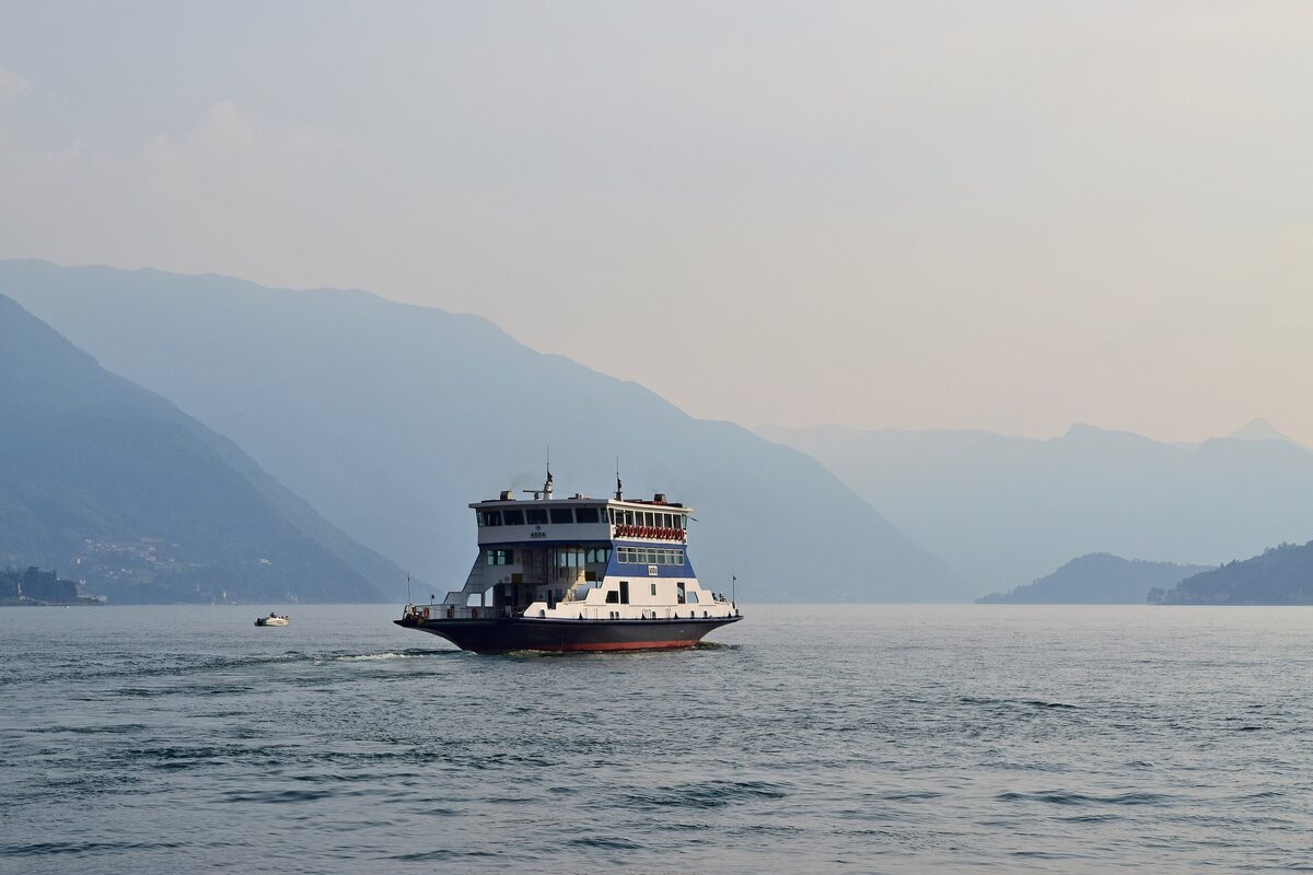 A passenger ferry crossing the hazy lake with mountains behind