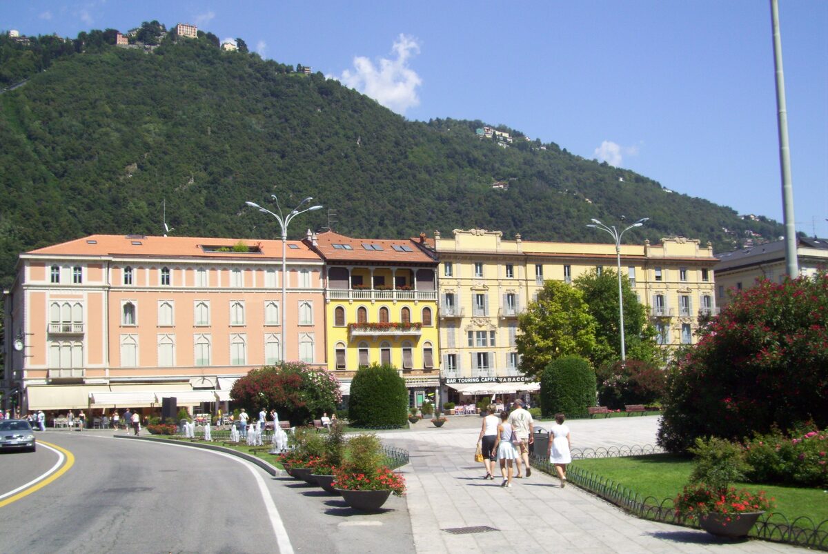Piazza Cavour in Como, with pink and yellow palazzi and a wooded hill behind
