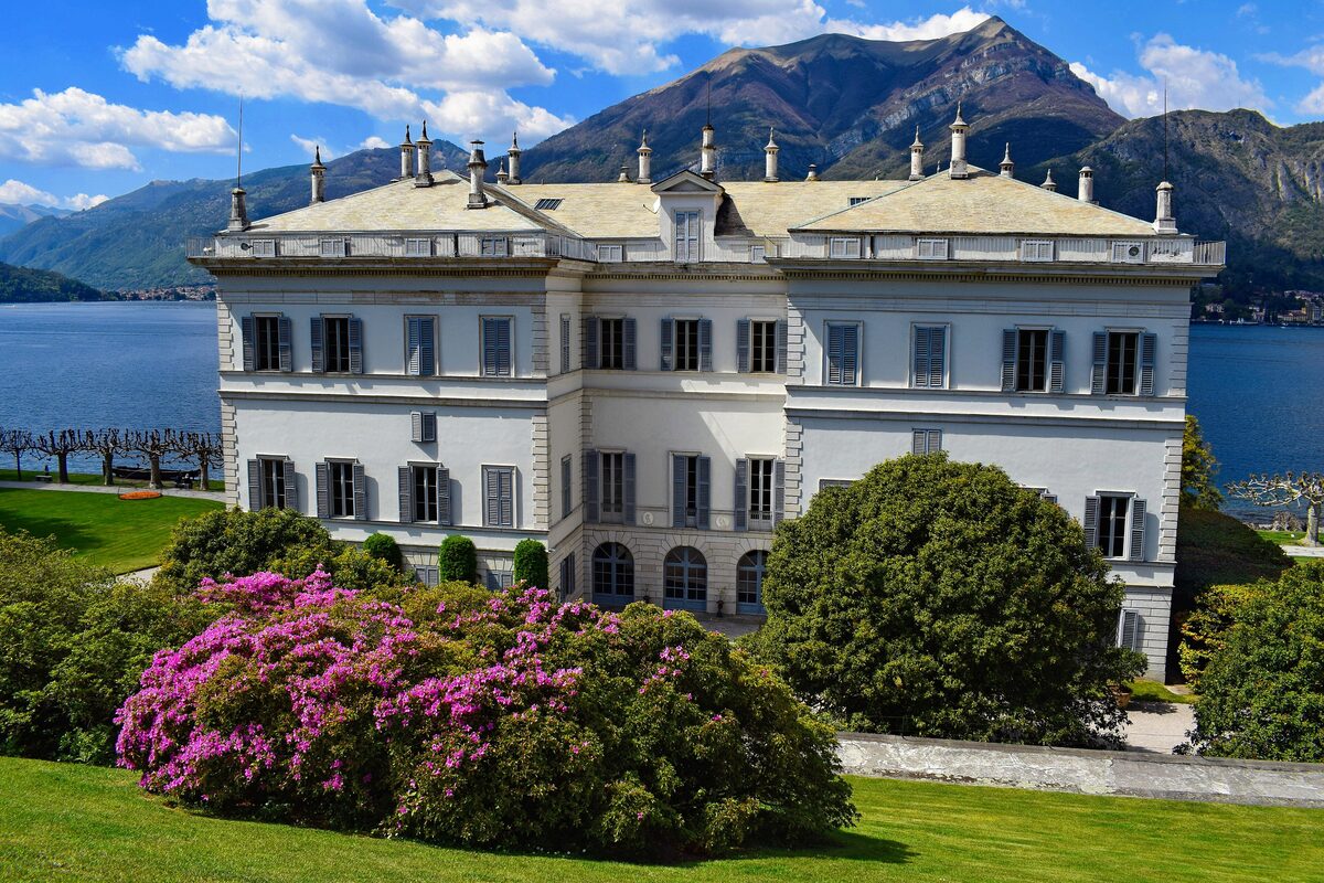The white facade of Villa Melzi behind a pink rhododendron and lawn