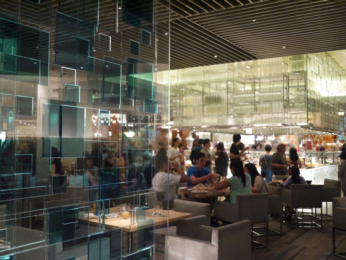 Diners at tables in the glass-walled dining room of a Las Vegas casino buffet, with food stations behind