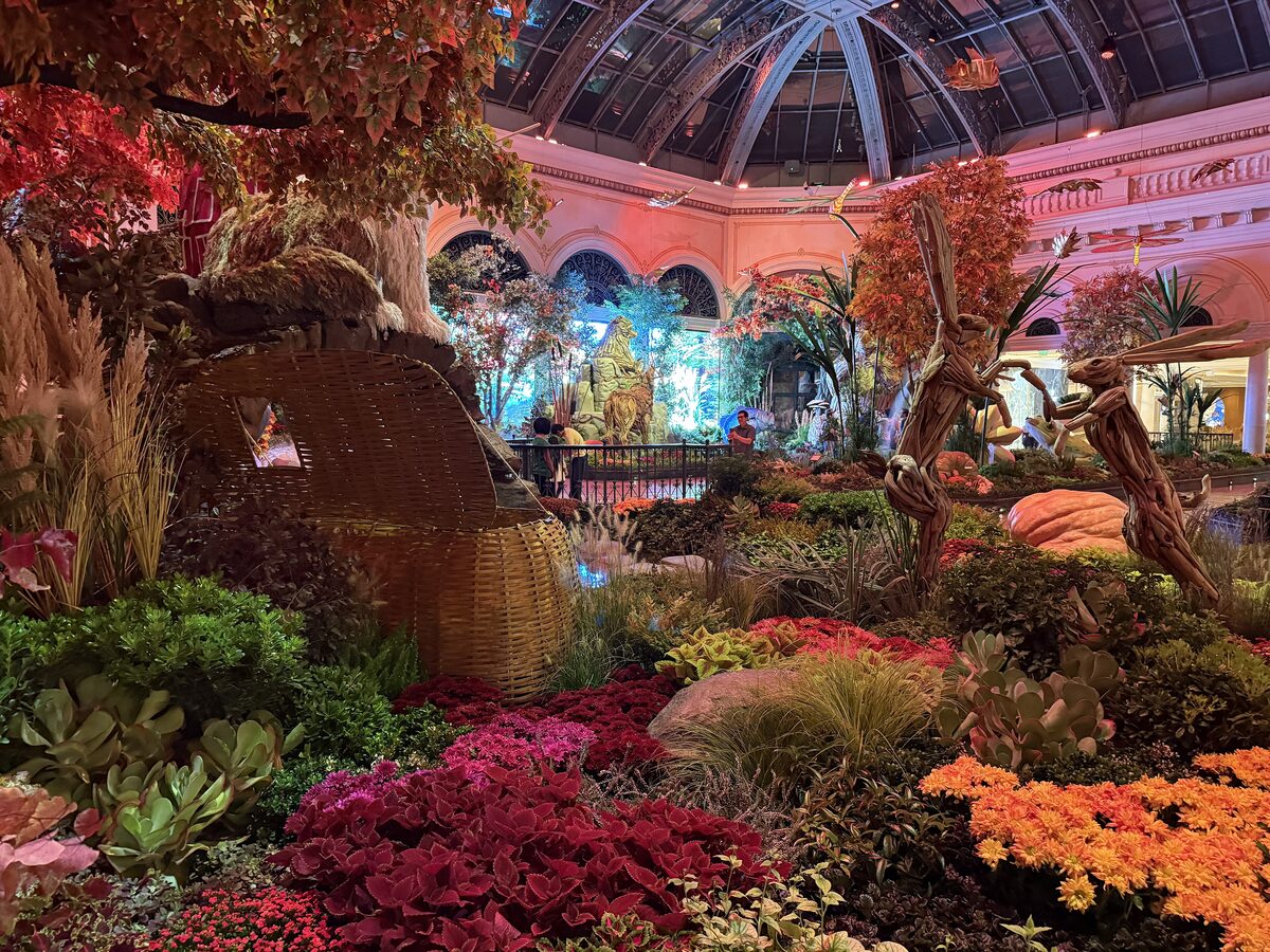 A seasonal flower display in the Bellagio Conservatory with red and orange plants, tree sculptures and the glass dome above