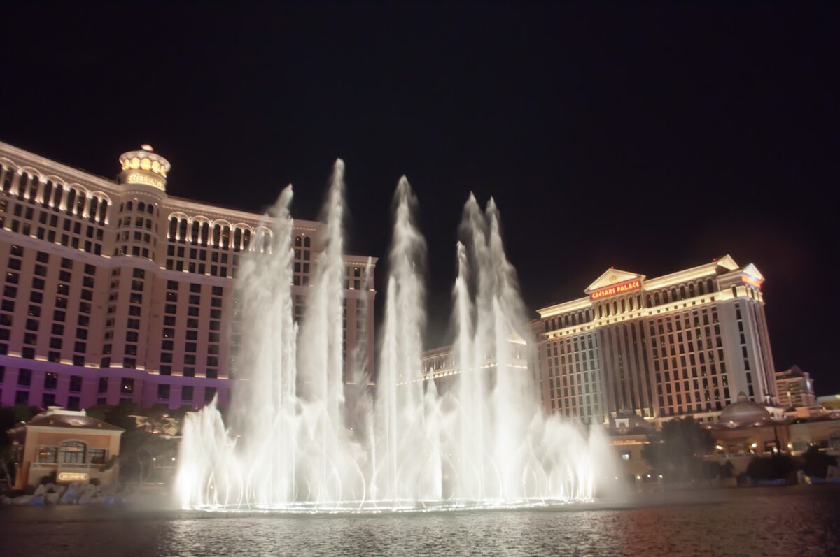 Jets of the Fountains of Bellagio shooting up at night in front of the Bellagio and Caesars Palace towers
