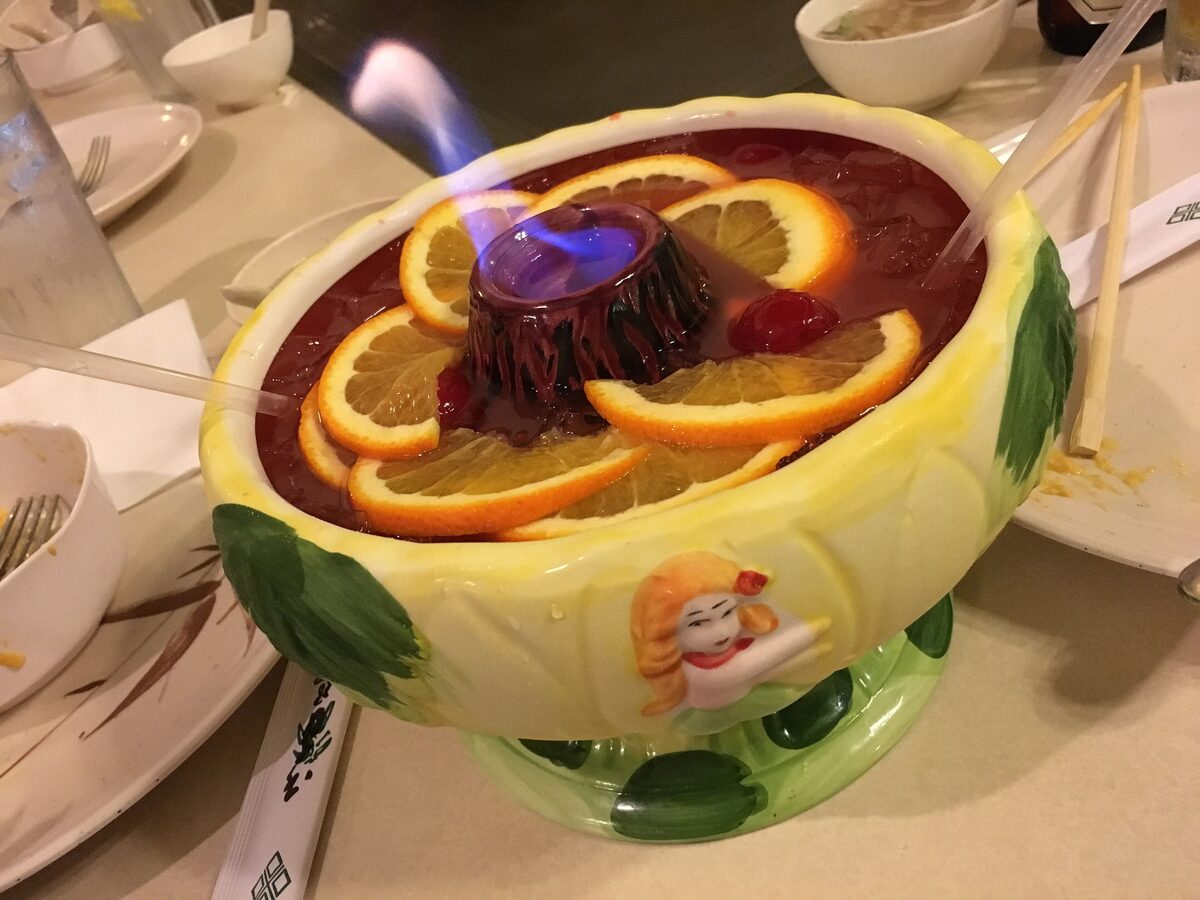 A flaming Scorpion Bowl in a ceramic bowl with orange slices and long straws