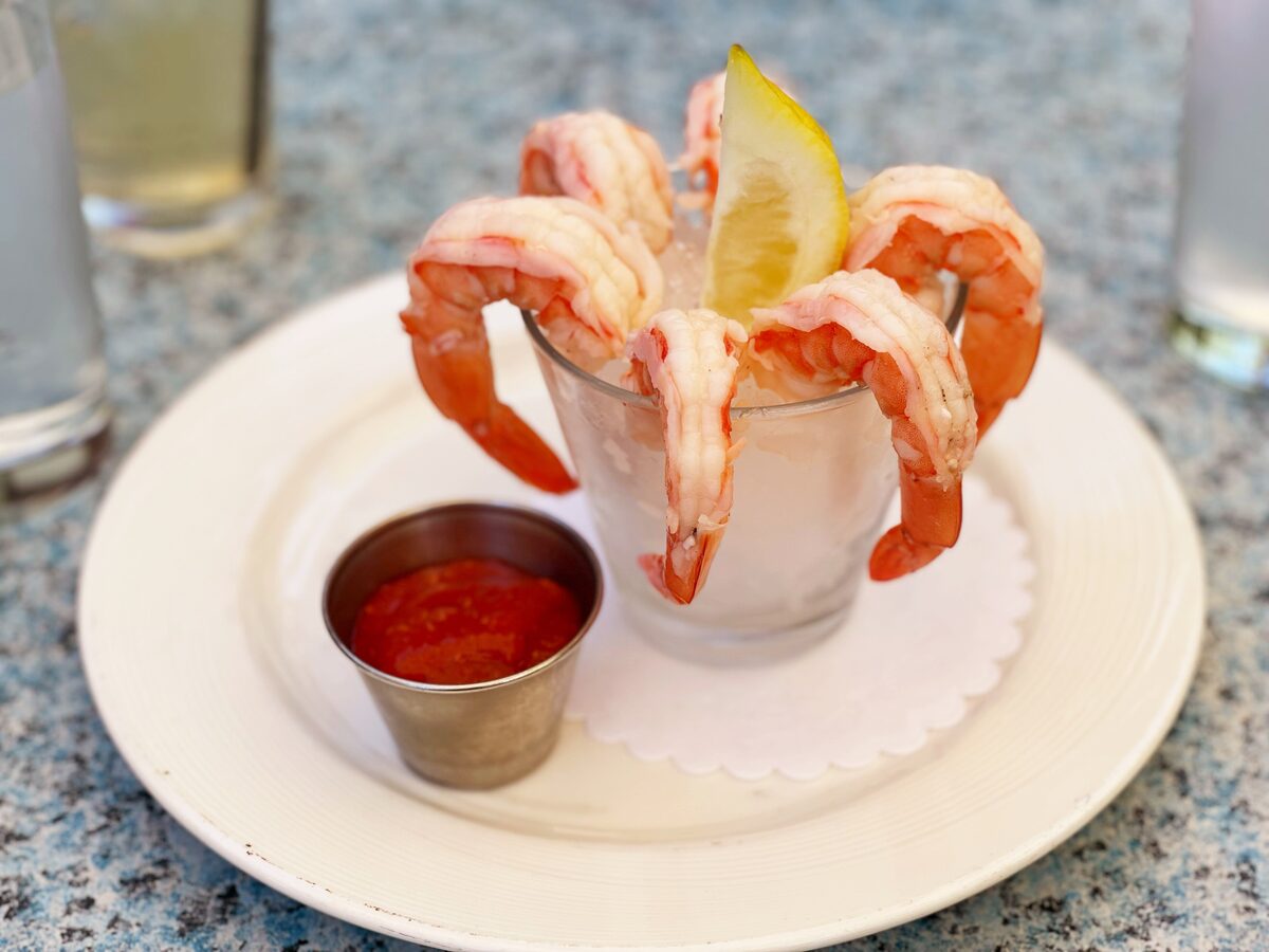 A classic shrimp cocktail, shrimp on a glass of ice with lemon and red sauce (an example, not Circa's own plate)