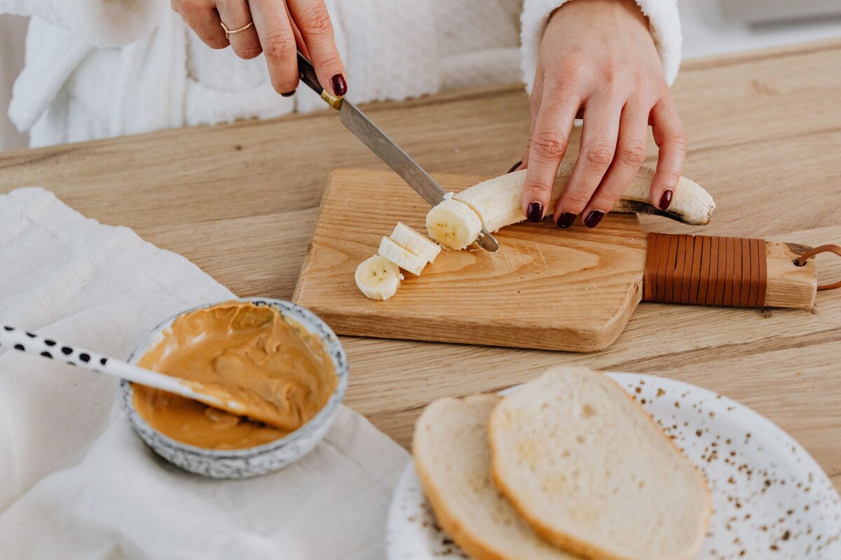 Sliced banana, peanut butter and bread on a wooden board