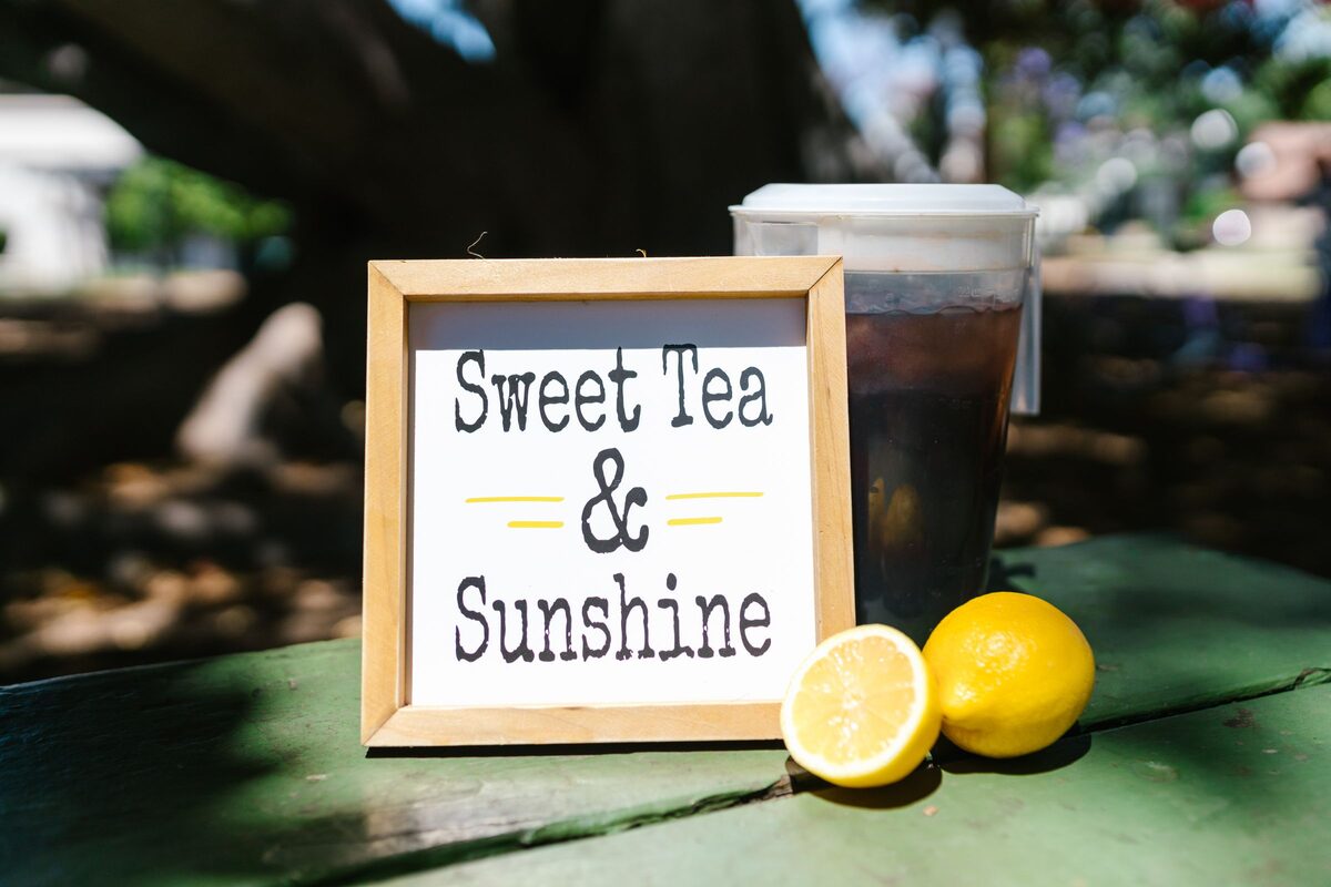 A pitcher of sweet tea beside a sign and two lemons