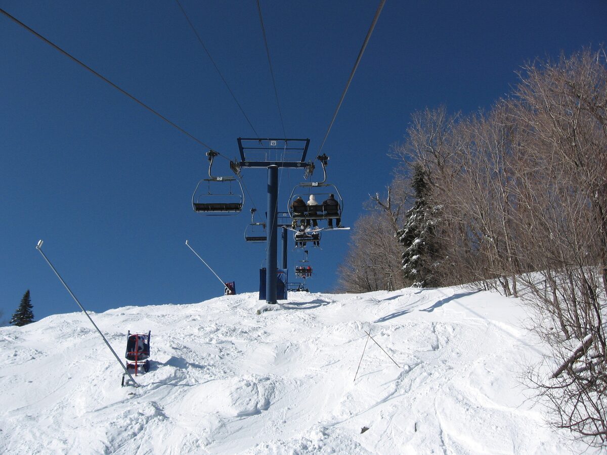 A four-seat chairlift rising over a snowy slope at Mont Tremblant under a deep blue sky