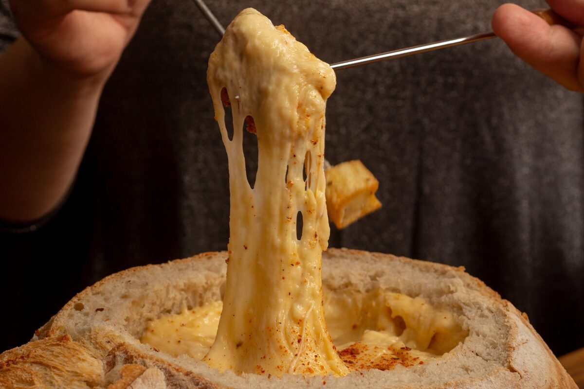 Melted cheese stretching from a fork out of a hollowed bread bowl of cheese fondue