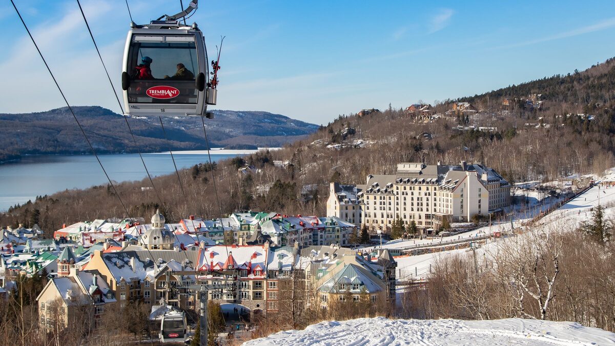 A Tremblant gondola cabin on its cable above the snowy pedestrian village, with Lac Tremblant and the hills behind