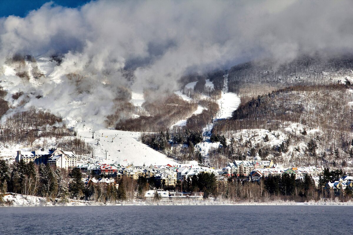 The resort village and the snowmaking clouds on the ski slopes above it, seen across Lac Tremblant in winter (the resort, not the Old Village itself)