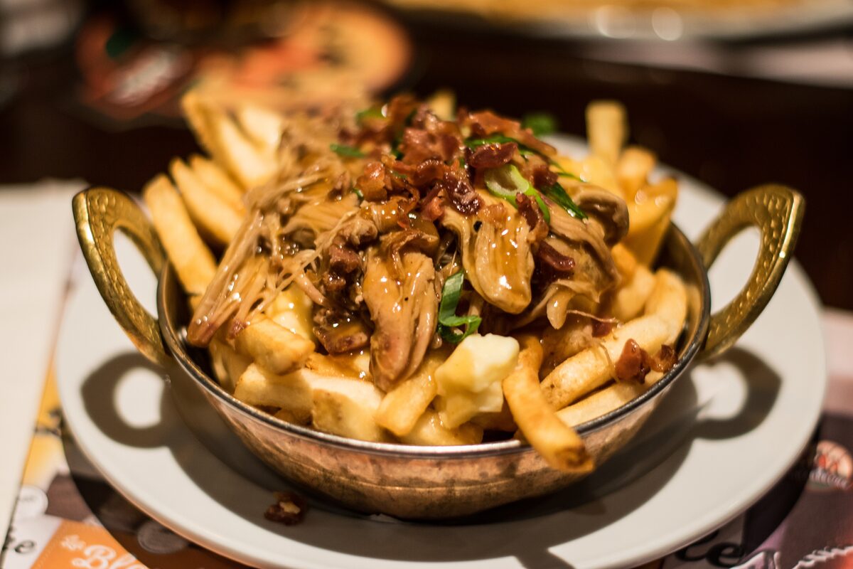 Poutine in a small copper pan: fries with pulled meat, bacon, gravy and white cheese curds
