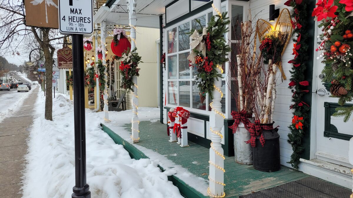 A snowy sidewalk on the main street of Saint-Jovite, lined with shop porches decorated with Christmas wreaths