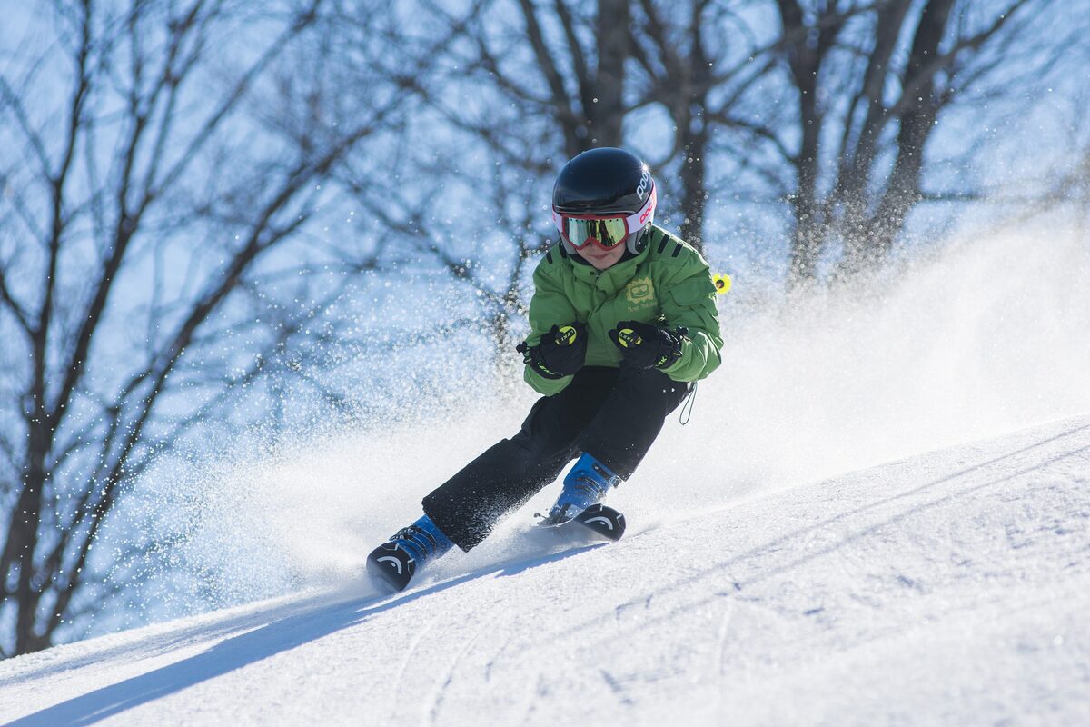 A skier in a green jacket carving a turn and throwing up powder on a snowy slope at Saint-Sauveur