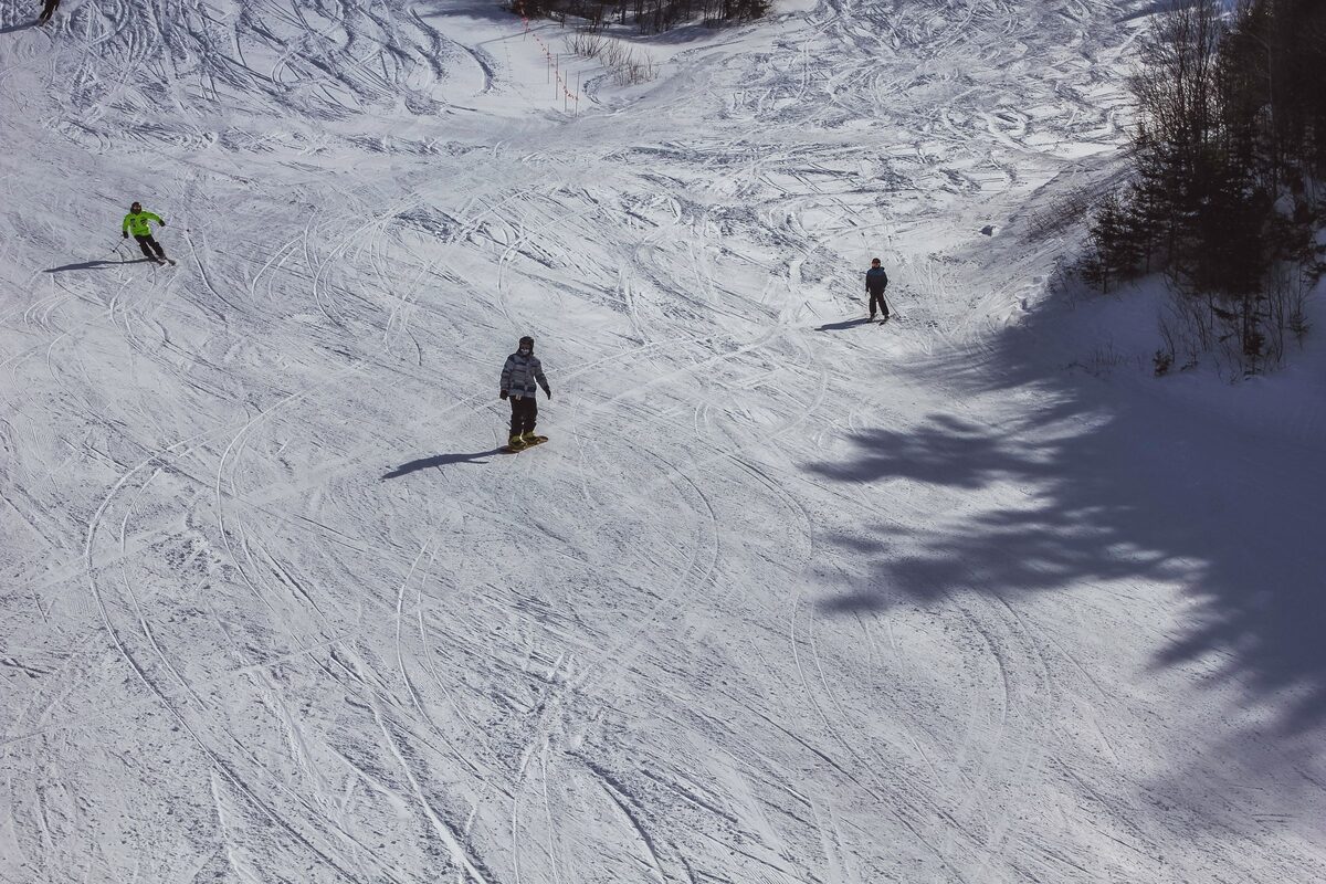Two skiers and a snowboarder on a wide, sunlit snowy slope at Mont-Tremblant