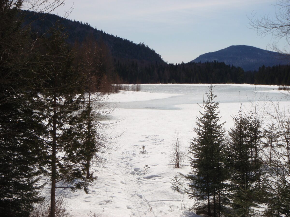 A snow-covered frozen lake (Lac Monroe) below wooded hills in Mont-Tremblant National Park in winter