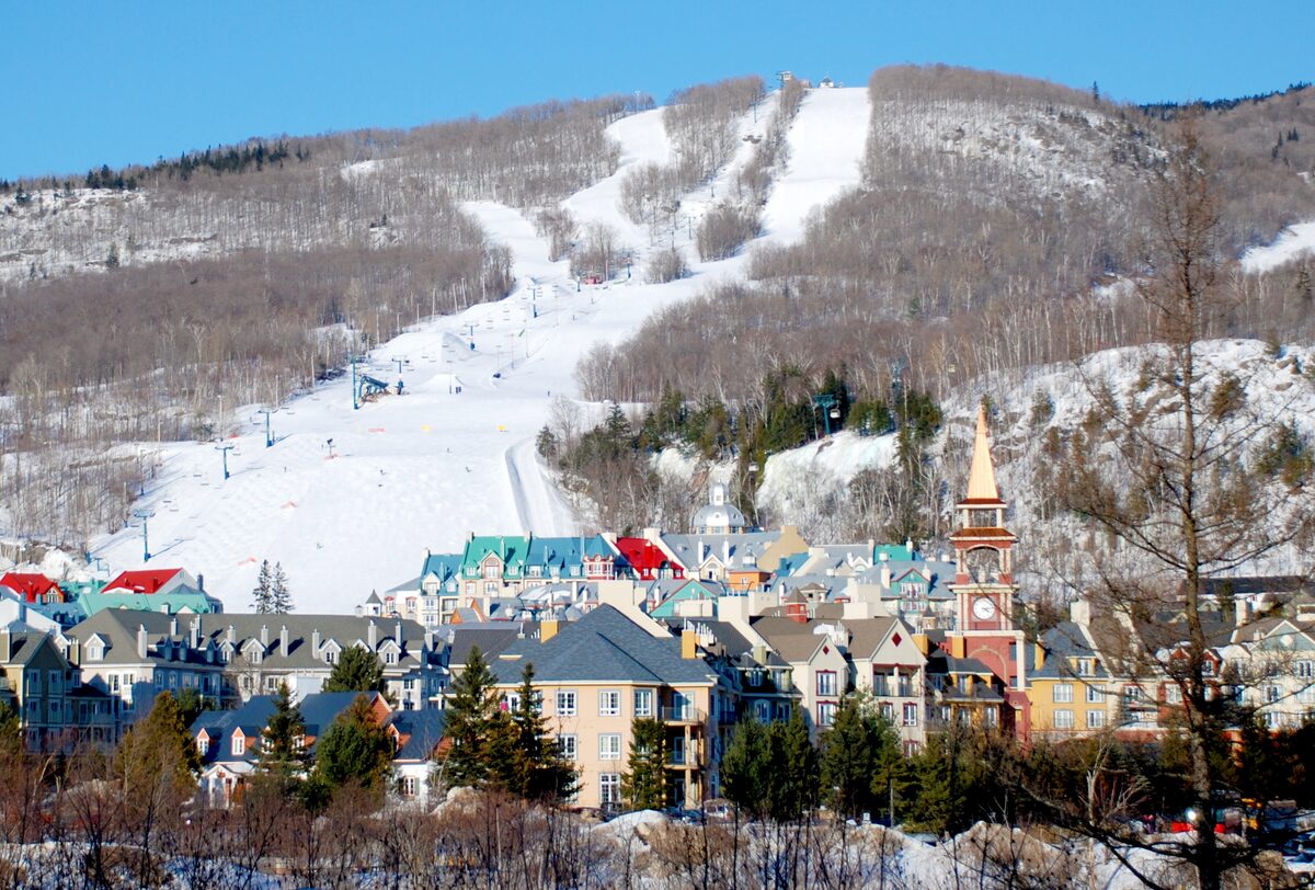 The Mont-Tremblant village below the snowy ski slopes above it, seen from outside the village on a bright winter day