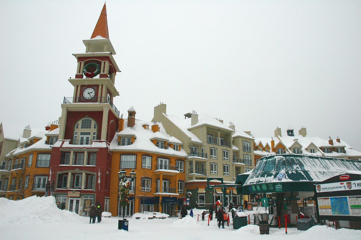 The red clock tower and the colorful snow-covered buildings of the Mont-Tremblant pedestrian village, with the gondola station on the right