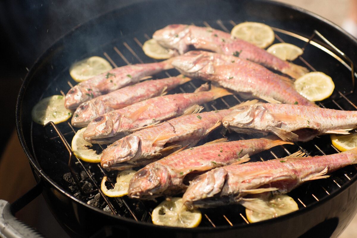 Whole red mullet grilling on a round barbecue with lemon slices