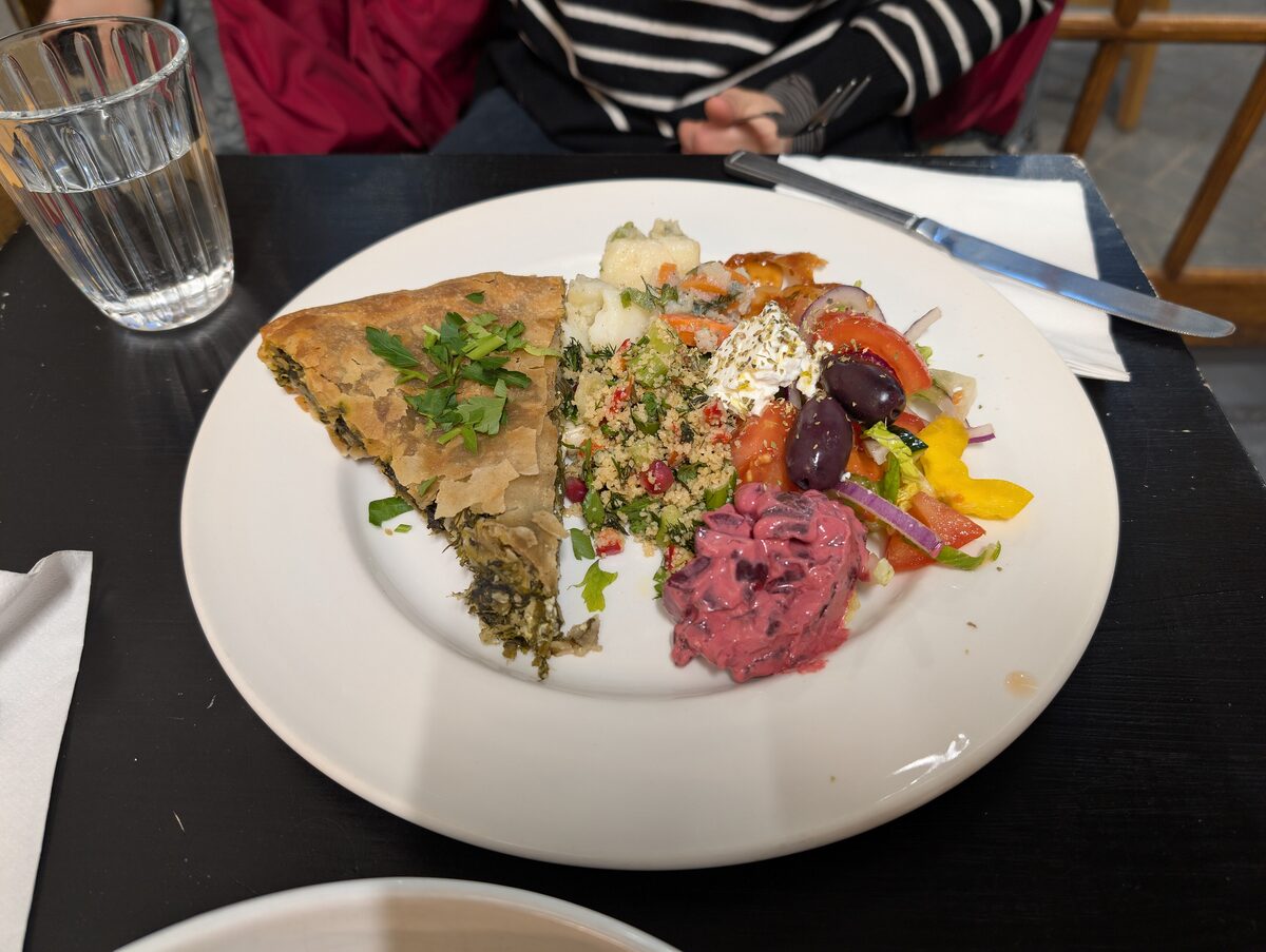 A slice of spanakopita beside a mezze spread on a dark plate