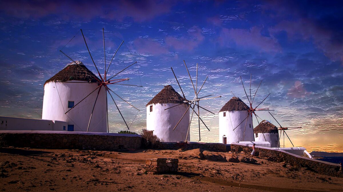 The white windmills of Mykonos on the hill at sunset, with the sky turning purple above them