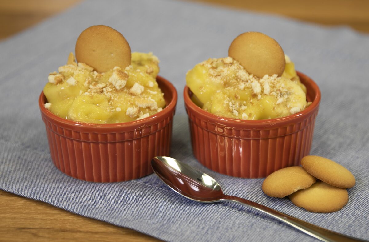 Two ramekins of banana pudding topped with vanilla wafers, with a spoon and more wafers beside them