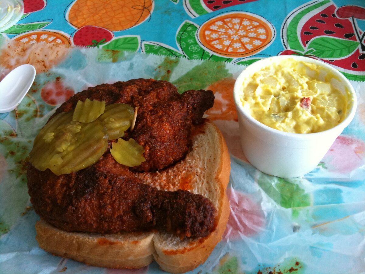 Nashville hot chicken, dark with cayenne paste, on white bread with pickle slices and a side of potato salad