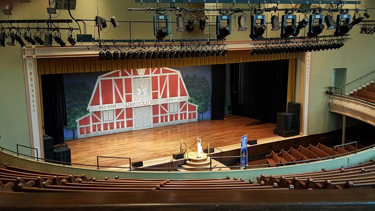 The stage of the Ryman Auditorium with the red barn backdrop, seen from the wooden pews and balcony