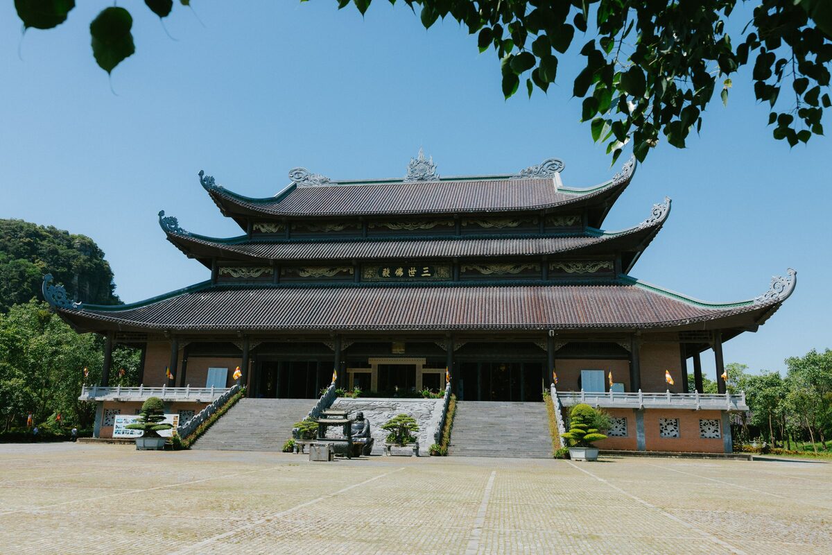 The three-tiered main hall of Bai Dinh Pagoda under a blue sky, seen from the courtyard