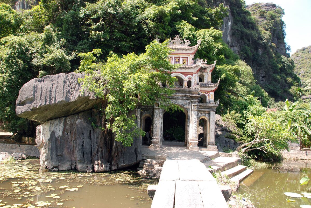 The gate of Bich Dong Pagoda in front of a huge rock, with a lily pond below