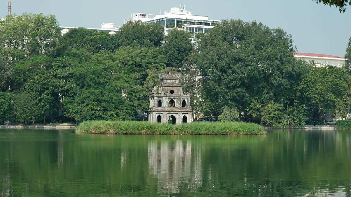 Turtle Tower on its islet in Hoan Kiem Lake, with green trees along the shore
