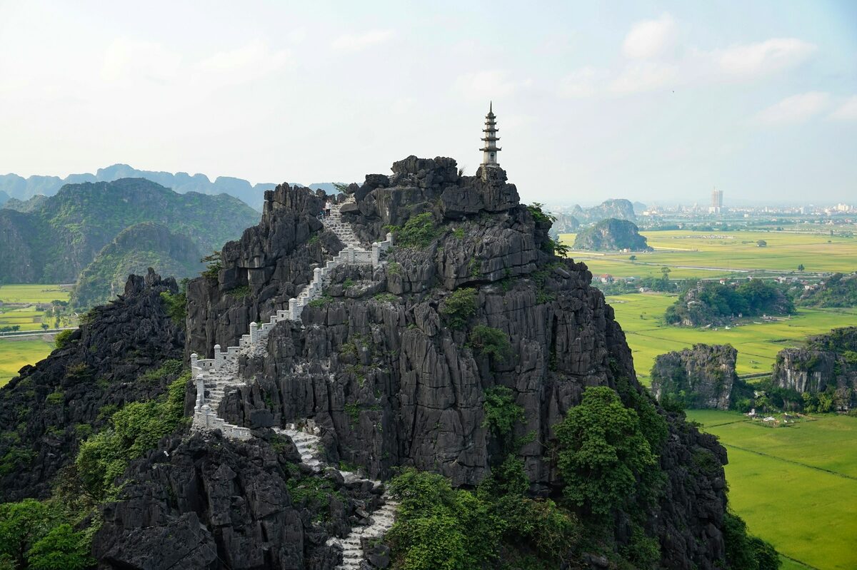 Stone steps climbing the rocky Mua Cave peak to a pagoda, with green rice fields and karst beyond