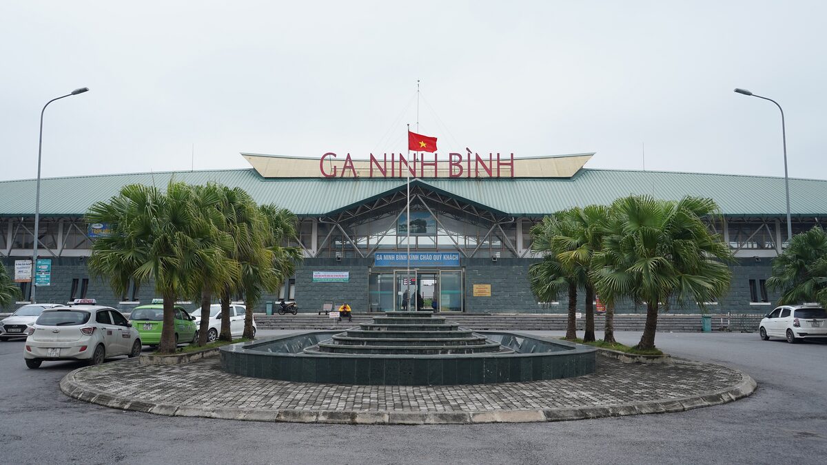 Ninh Binh railway station with its red sign, palm trees and a fountain roundabout