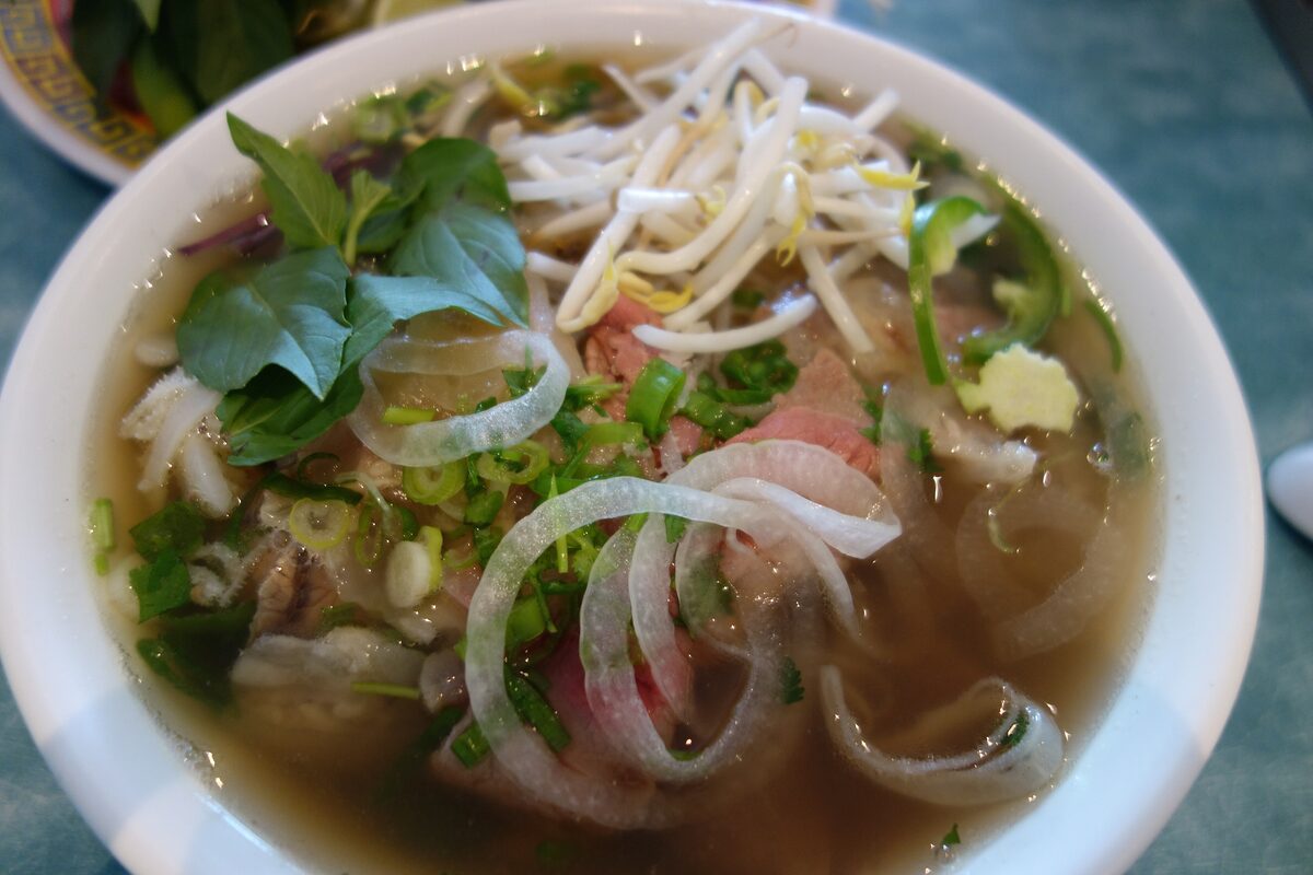 A bowl of beef pho with rice noodles, slices of beef, onion and fresh herbs