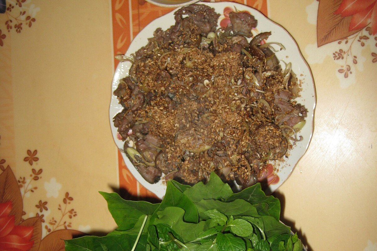 Stir-fried goat meat with sesame seeds on a plate, with fresh herb leaves