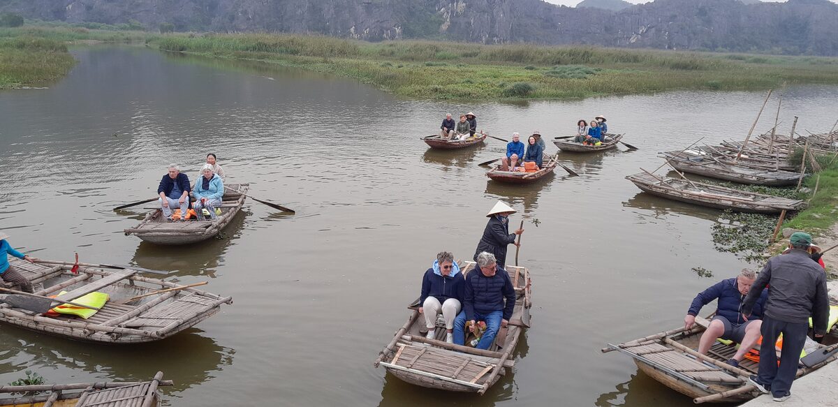 Wooden boats with tourists on the Van Long wetland, with limestone hills on the horizon