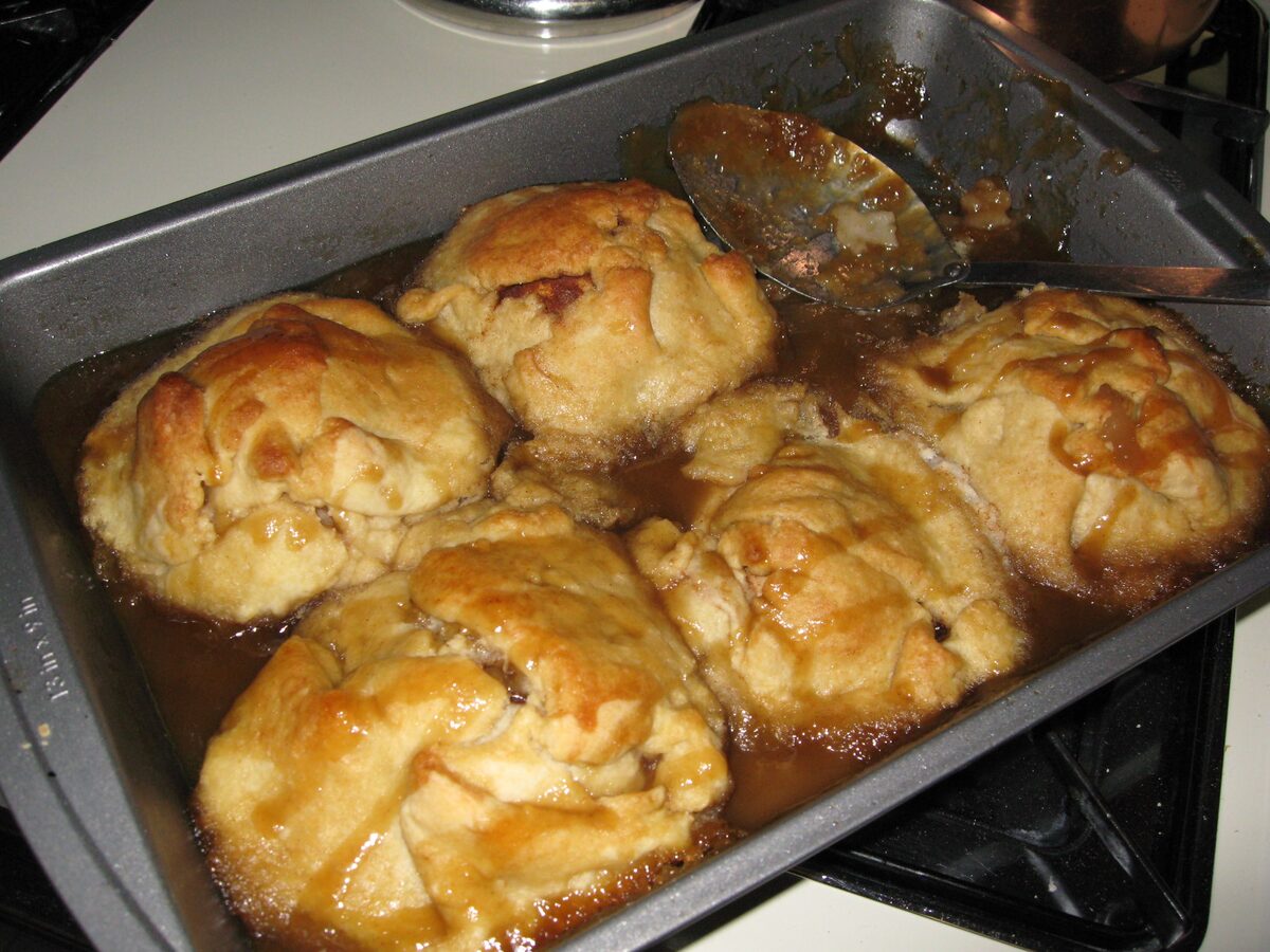 A baking tray of golden apple dumplings in caramel syrup