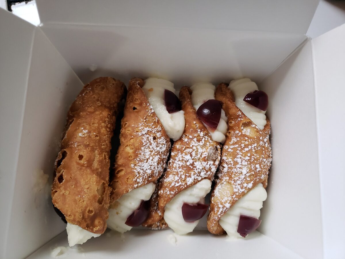 Four cannoli filled with ricotta cream and dusted with sugar in a box