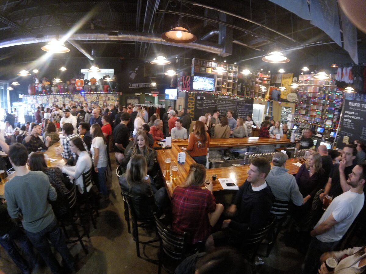 A crowded bar in the Yards Brewing taproom under industrial lamps