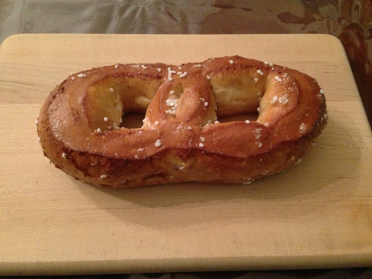 A golden Philadelphia soft pretzel sprinkled with salt on a wooden board