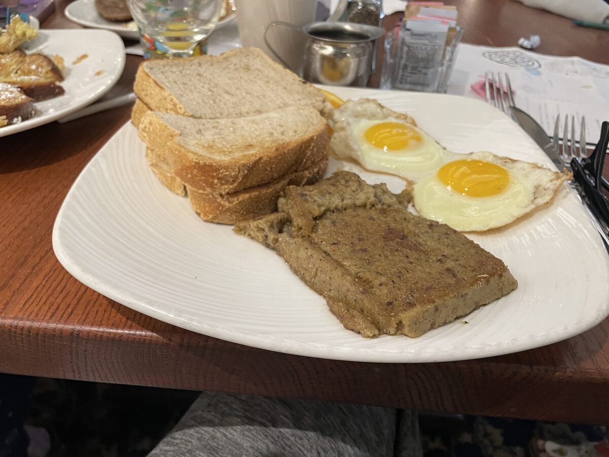 A slice of fried scrapple on a plate with two fried eggs and toast