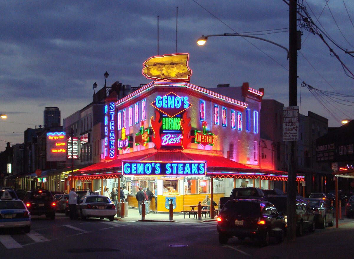 Geno's Steaks glowing in red, blue and orange neon at dusk