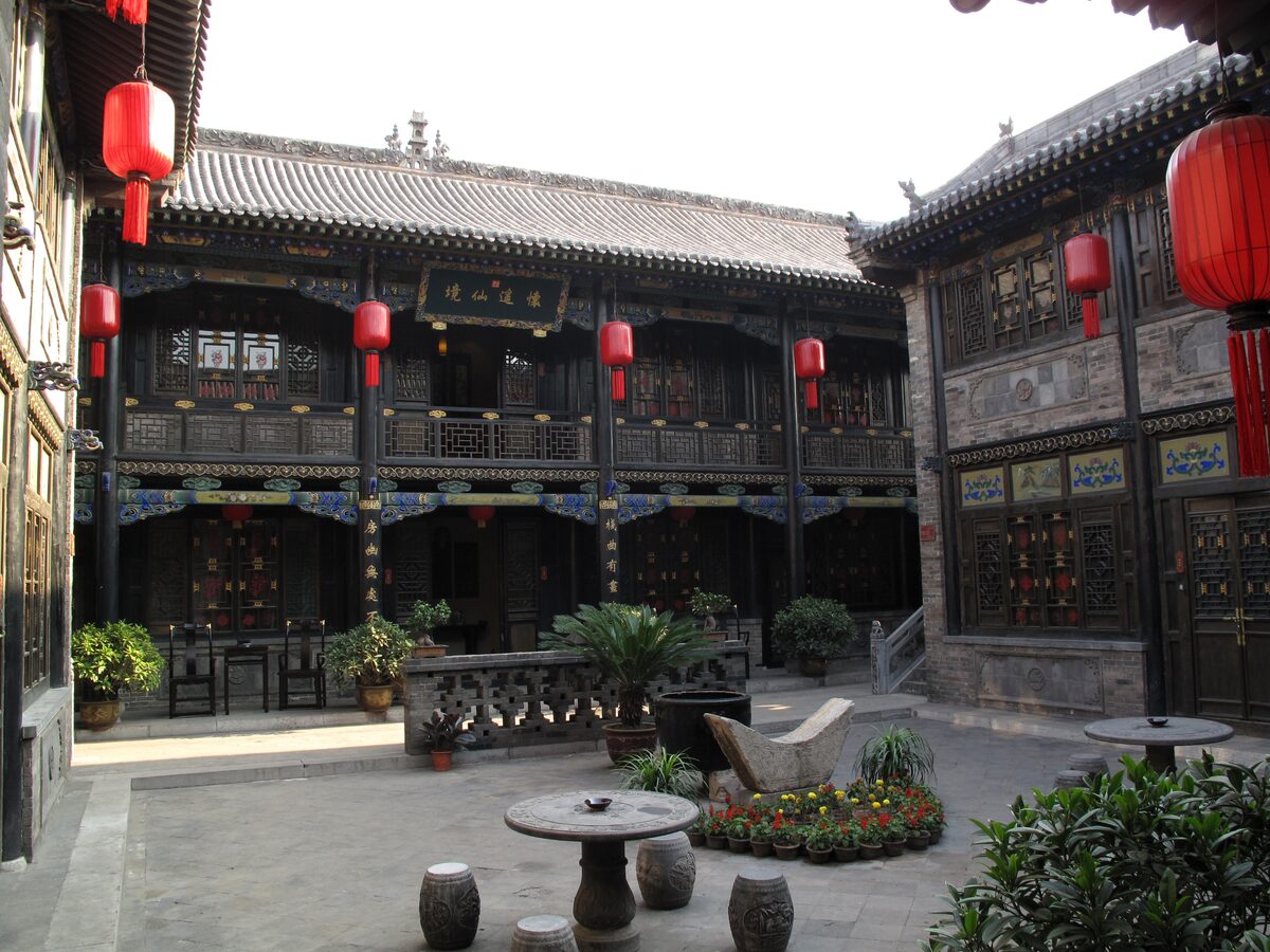 A two-storey courtyard house in Pingyao with carved wooden balconies, red lanterns and stone tables in the yard