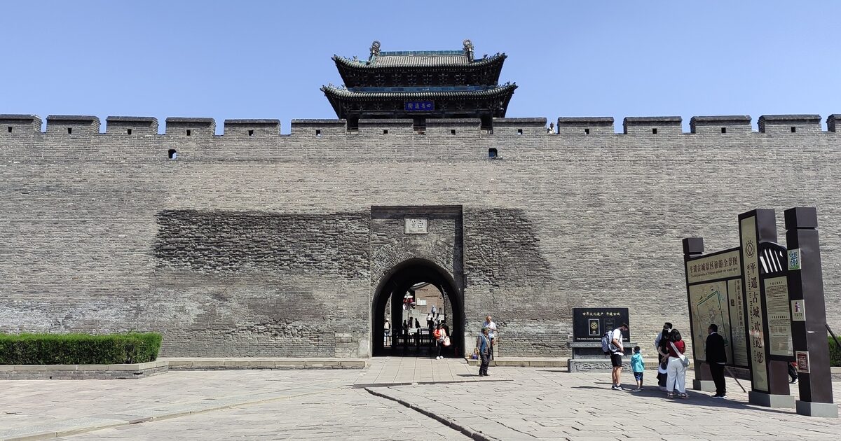 The Yingxun Gate tower rising above the grey brick city wall of Pingyao under a clear blue sky
