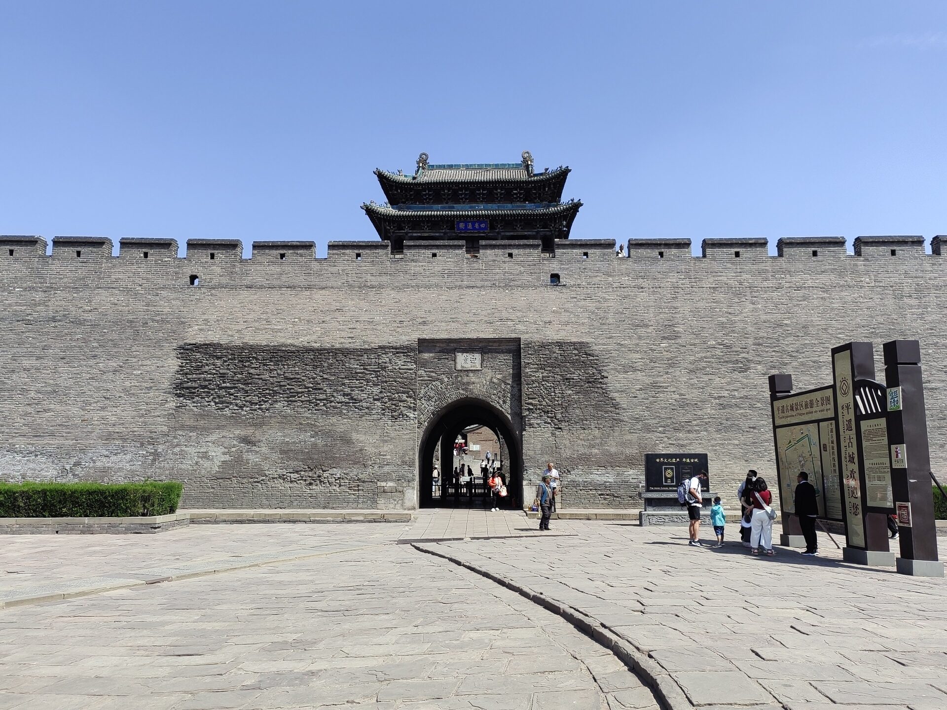The Yingxun Gate tower rising above the grey brick city wall of Pingyao under a clear blue sky