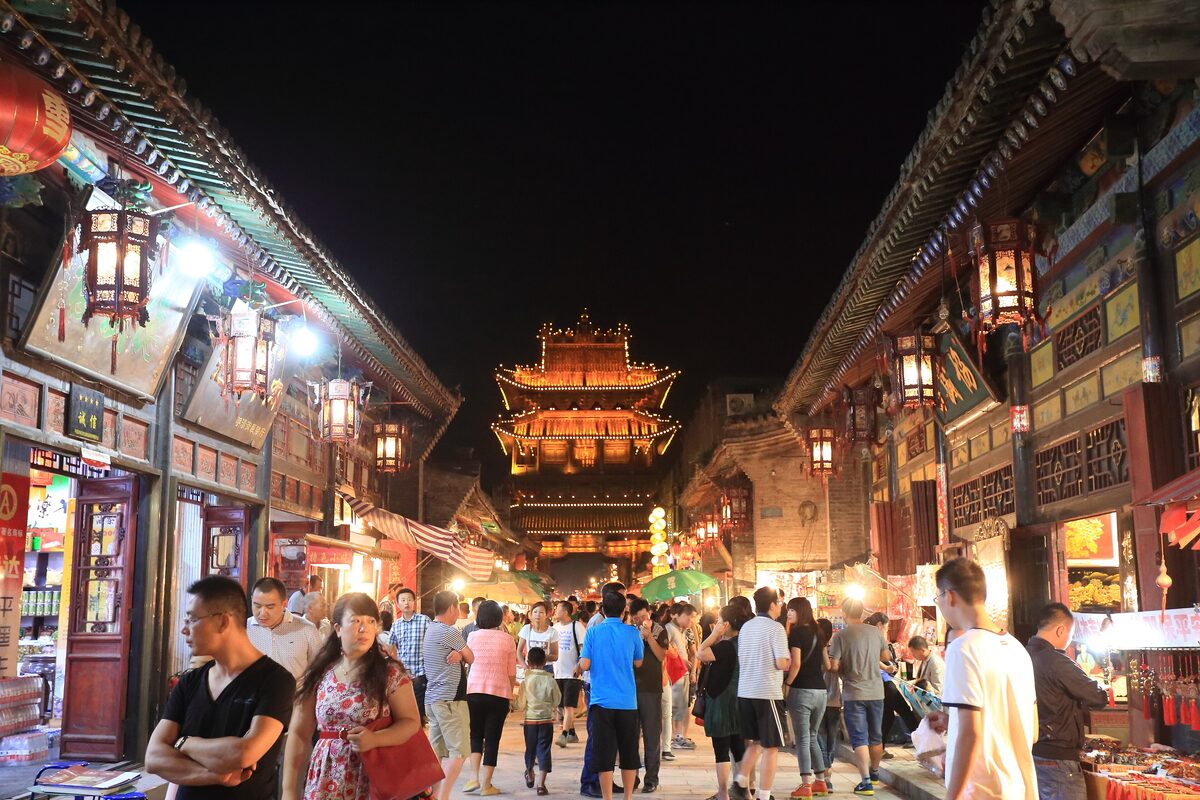 A crowd of visitors on the lantern-lit main street at night, with the lit-up Market Tower at the end